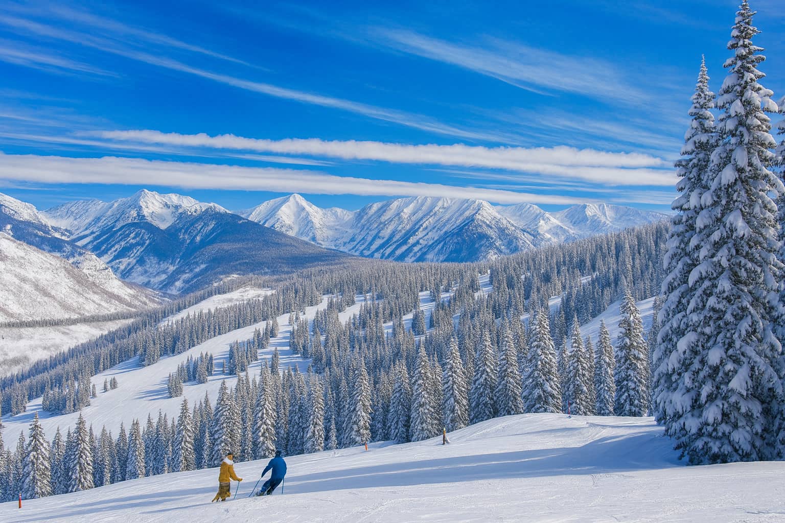 Aspen fractional ownership skiers on the pistes with the mountains in the backdrop